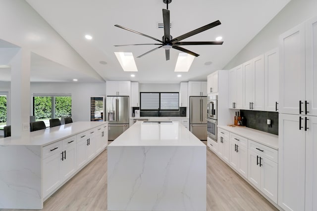 kitchen featuring white cabinets, a kitchen island, lofted ceiling with skylight, and appliances with stainless steel finishes