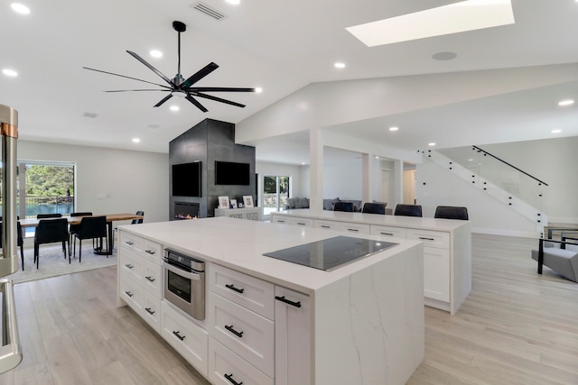 kitchen featuring appliances with stainless steel finishes, vaulted ceiling with skylight, white cabinets, light hardwood / wood-style floors, and a large island