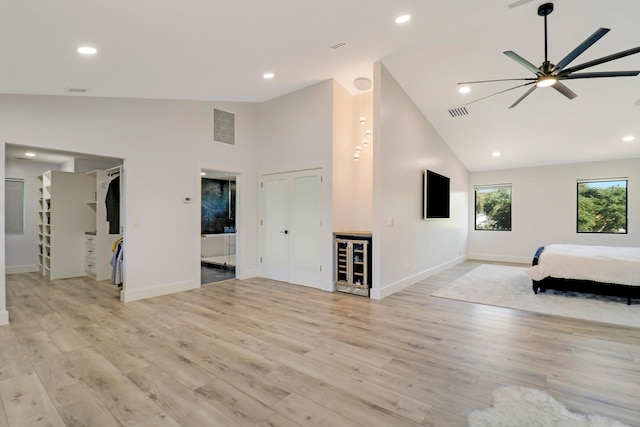 unfurnished living room featuring wine cooler, ceiling fan, high vaulted ceiling, and light hardwood / wood-style floors