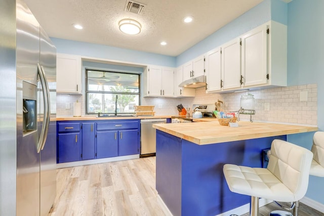 kitchen featuring wooden counters, appliances with stainless steel finishes, a kitchen bar, blue cabinetry, and white cabinetry