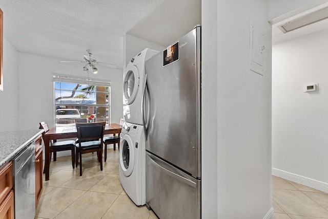 laundry room featuring ceiling fan, stacked washing maching and dryer, a textured ceiling, and light tile patterned floors