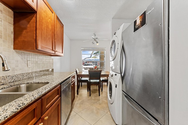 kitchen with light stone countertops, stacked washing maching and dryer, tasteful backsplash, stainless steel appliances, and ceiling fan