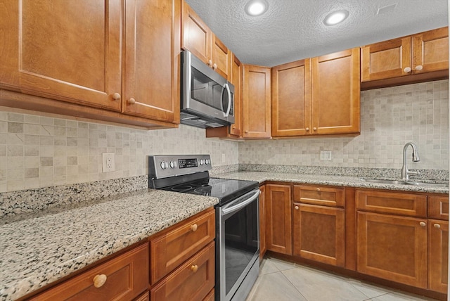 kitchen with sink, stainless steel appliances, light stone counters, a textured ceiling, and light tile patterned floors