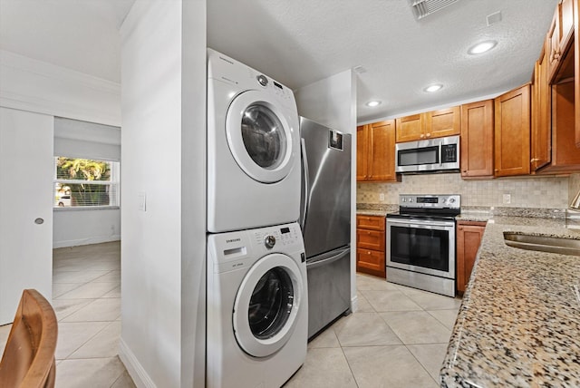 kitchen with light stone countertops, stacked washer and dryer, decorative backsplash, light tile patterned floors, and appliances with stainless steel finishes