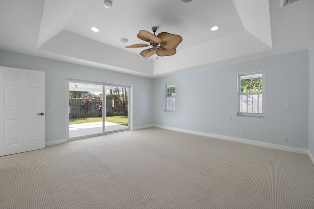 empty room with a tray ceiling, plenty of natural light, and ceiling fan