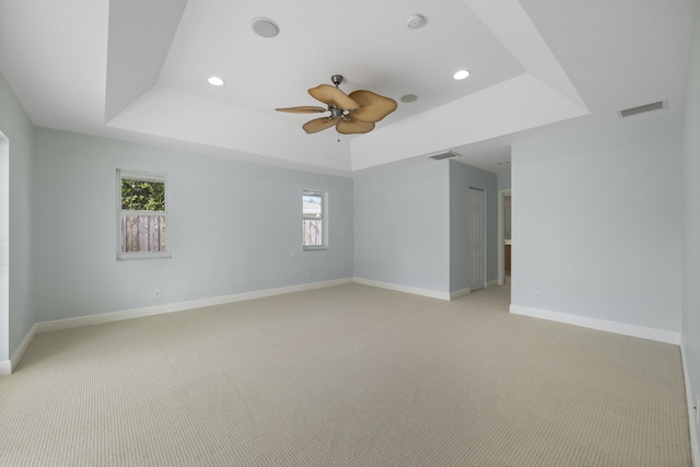 empty room with light carpet, a tray ceiling, and ceiling fan