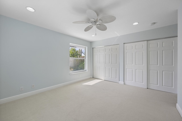 unfurnished bedroom with ceiling fan, light carpet, and two closets