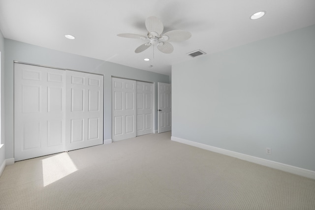 unfurnished bedroom featuring ceiling fan, light colored carpet, and multiple closets