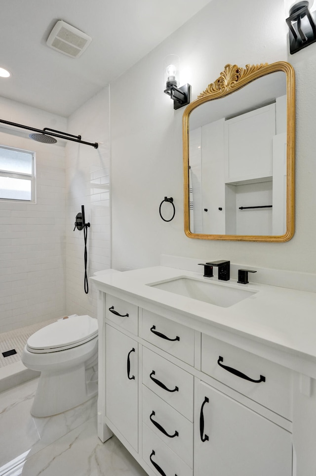 bathroom featuring a tile shower, vanity, and toilet