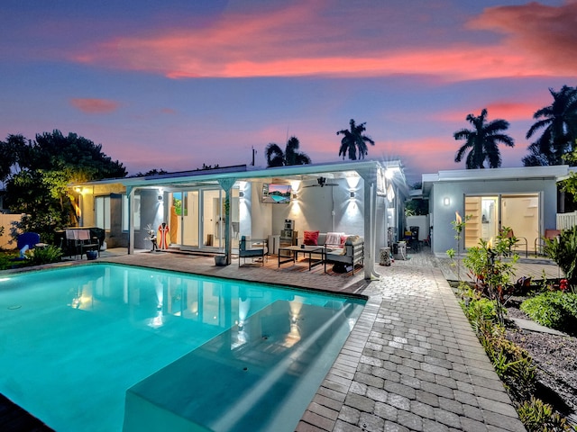 pool at dusk with outdoor lounge area, ceiling fan, a patio, and an outdoor structure