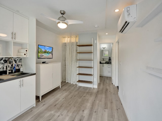 unfurnished dining area featuring ceiling fan, light wood-type flooring, an AC wall unit, and sink