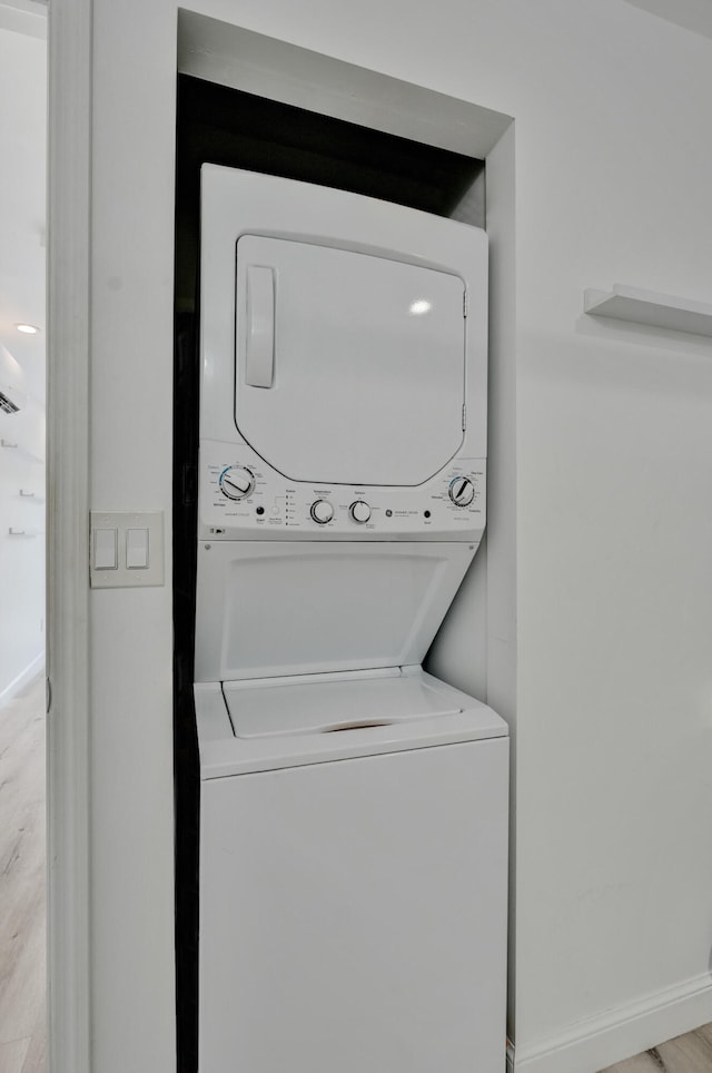 laundry room featuring stacked washer / dryer and light hardwood / wood-style flooring