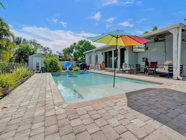 view of swimming pool featuring ceiling fan, a patio area, and a storage shed