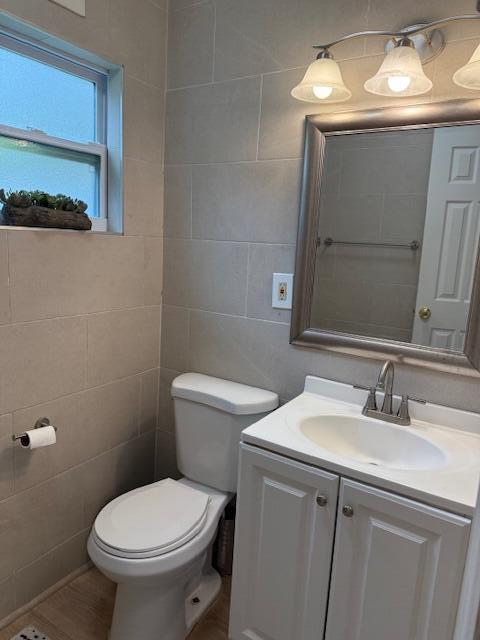 bathroom with toilet, vanity, and tile walls