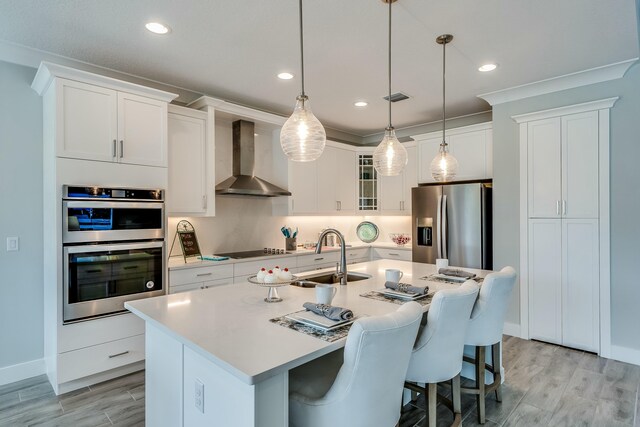 kitchen featuring sink, hanging light fixtures, wall chimney exhaust hood, an island with sink, and appliances with stainless steel finishes