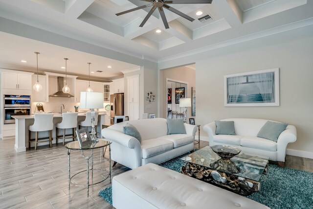 living room featuring ornamental molding, coffered ceiling, sink, beamed ceiling, and light hardwood / wood-style floors