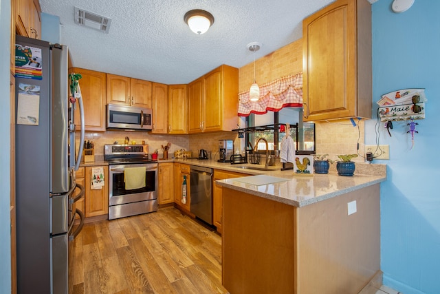 kitchen featuring decorative light fixtures, light stone counters, kitchen peninsula, stainless steel appliances, and light hardwood / wood-style flooring