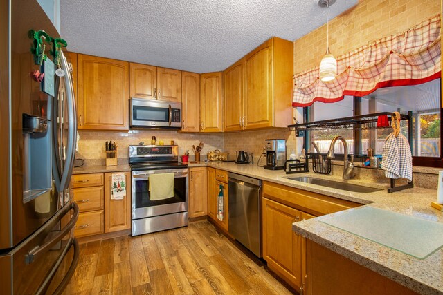 kitchen with kitchen peninsula, appliances with stainless steel finishes, decorative light fixtures, light wood-type flooring, and sink