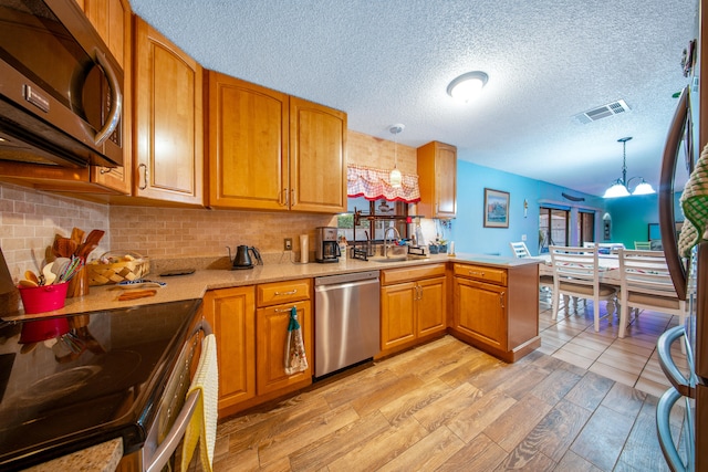 kitchen with sink, a chandelier, kitchen peninsula, pendant lighting, and stainless steel appliances