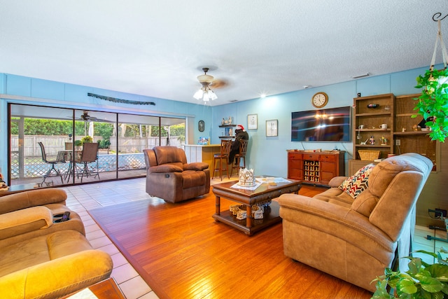 living room with hardwood / wood-style flooring, ceiling fan, and a textured ceiling