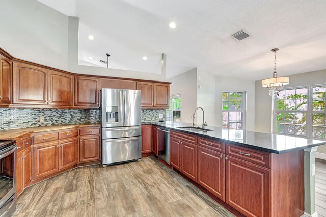 kitchen with dark stone countertops, light wood-type flooring, backsplash, and appliances with stainless steel finishes