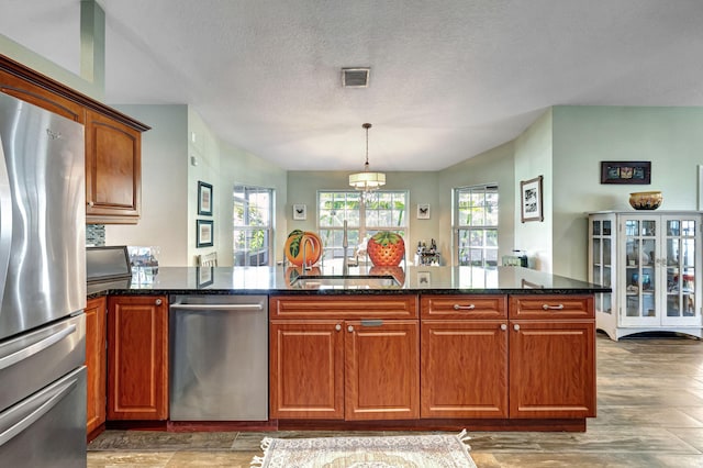 kitchen featuring a textured ceiling, stainless steel appliances, pendant lighting, dark stone countertops, and dark hardwood / wood-style floors