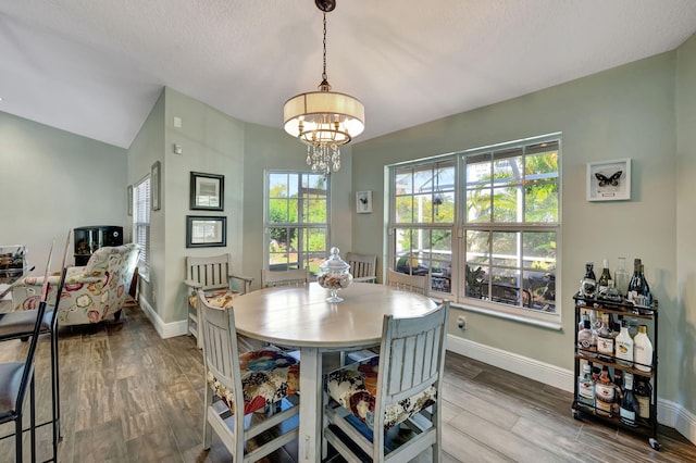 dining space featuring hardwood / wood-style flooring, a healthy amount of sunlight, vaulted ceiling, and an inviting chandelier