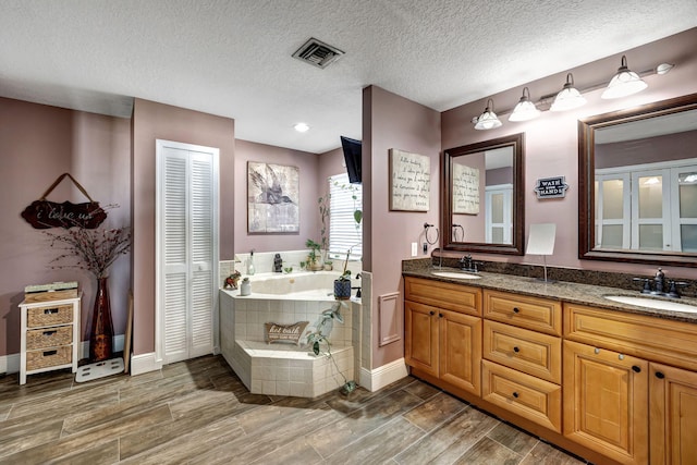 bathroom featuring wood-type flooring, vanity, tiled bath, and a textured ceiling