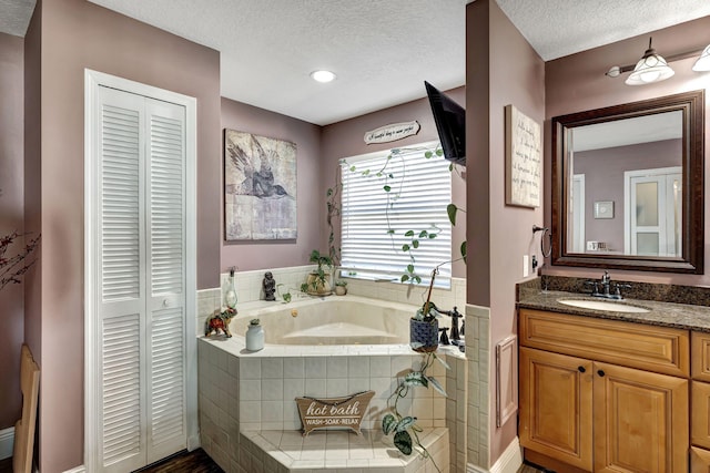 bathroom featuring a textured ceiling, vanity, and tiled tub