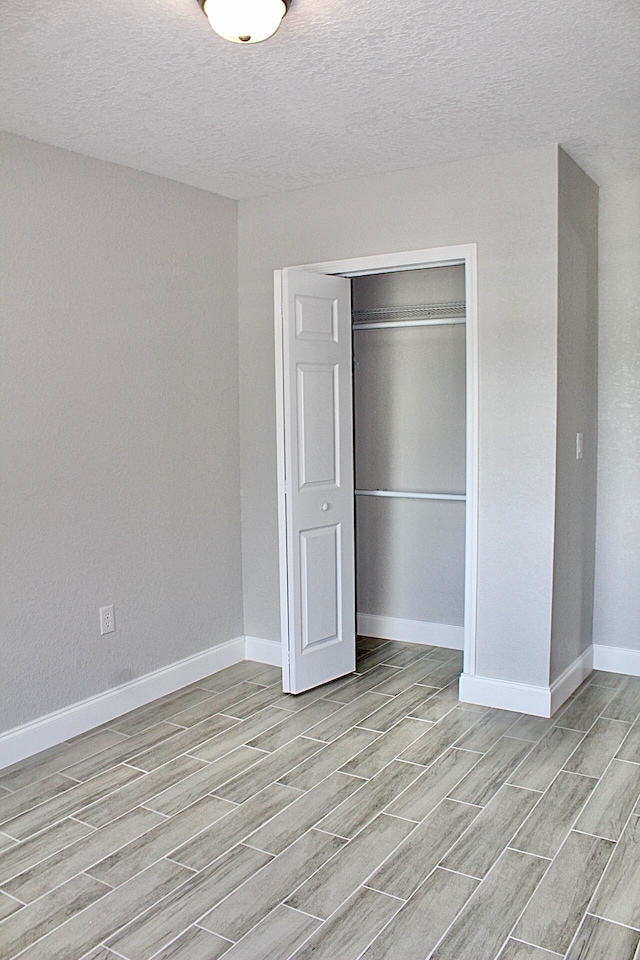 unfurnished bedroom with light wood-type flooring, a textured ceiling, and a closet