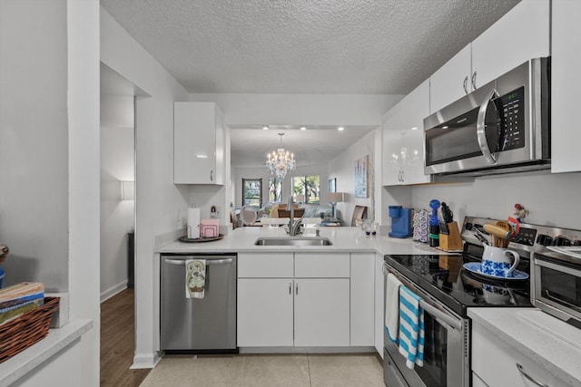 kitchen with hanging light fixtures, stainless steel appliances, a chandelier, white cabinets, and light wood-type flooring