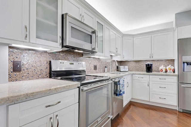 kitchen with stainless steel appliances, tasteful backsplash, light stone counters, wood-type flooring, and white cabinets