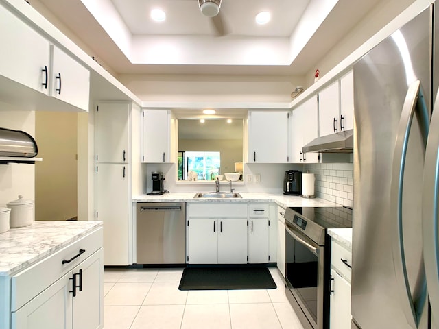 kitchen featuring appliances with stainless steel finishes, a raised ceiling, sink, light tile patterned floors, and white cabinetry