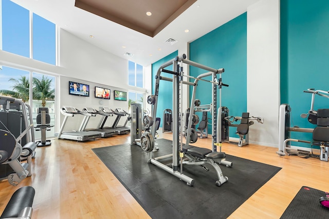 gym featuring hardwood / wood-style floors, a raised ceiling, and a high ceiling