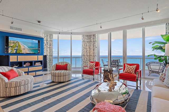 living room with track lighting, expansive windows, a textured ceiling, and a water view