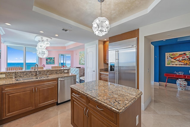 kitchen with brown cabinets, appliances with stainless steel finishes, a raised ceiling, and a sink