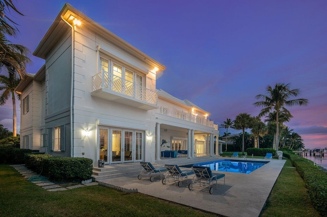 back house at dusk with a patio area, a balcony, and french doors