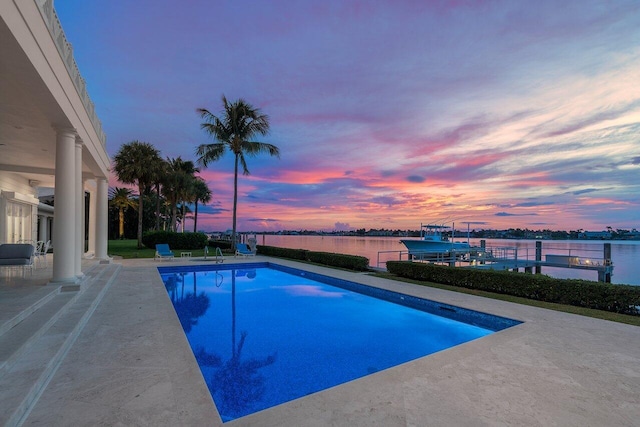 pool at dusk with a patio and a water view