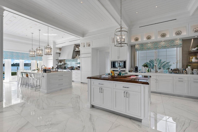 kitchen with butcher block counters, wooden ceiling, pendant lighting, a center island with sink, and white cabinets