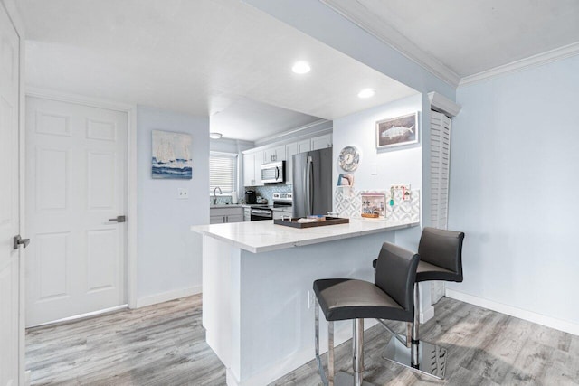 kitchen featuring sink, kitchen peninsula, a breakfast bar, appliances with stainless steel finishes, and light wood-type flooring