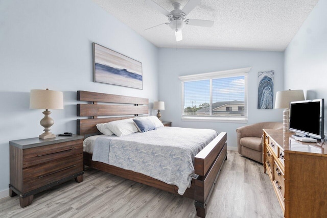 bedroom with a textured ceiling, ceiling fan, light hardwood / wood-style flooring, and lofted ceiling