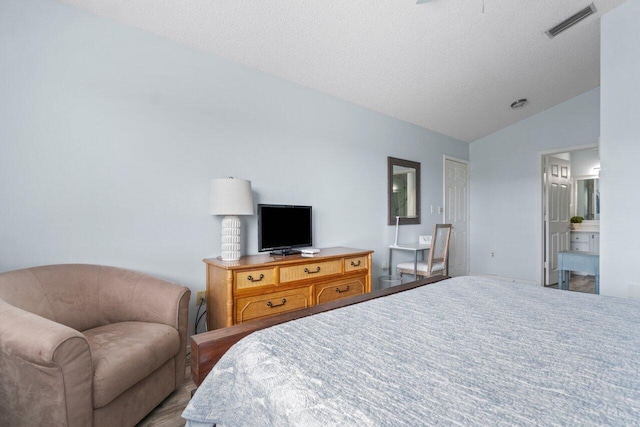 bedroom with ensuite bathroom, lofted ceiling, and a textured ceiling