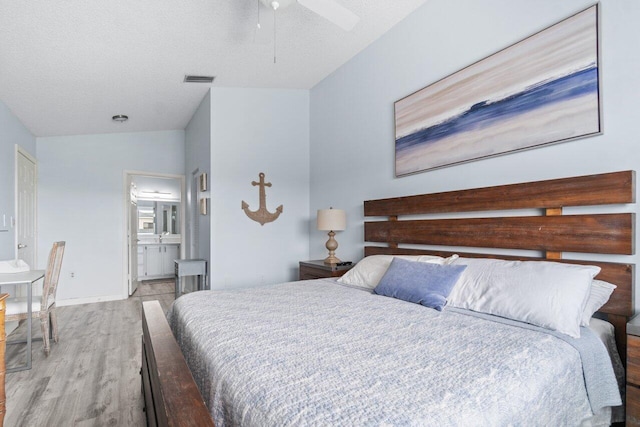 bedroom with ceiling fan, ensuite bathroom, light hardwood / wood-style floors, lofted ceiling, and a textured ceiling