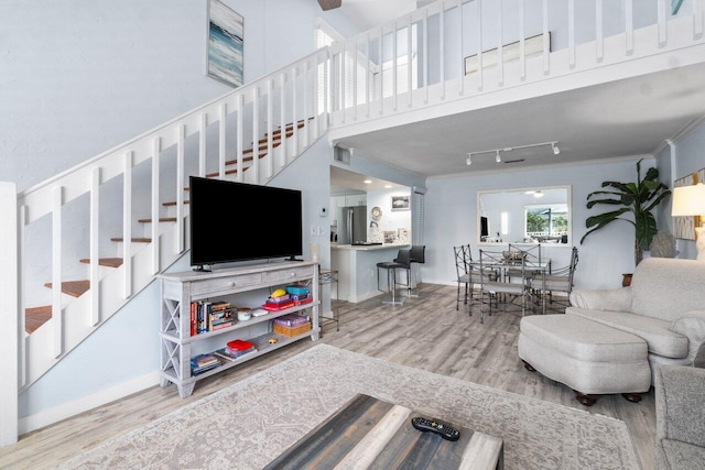 living room with ceiling fan, hardwood / wood-style floors, a towering ceiling, track lighting, and ornamental molding