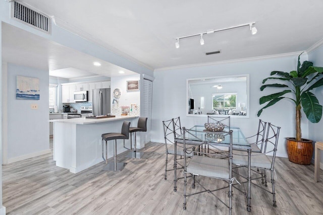 dining space featuring rail lighting, light hardwood / wood-style floors, and crown molding