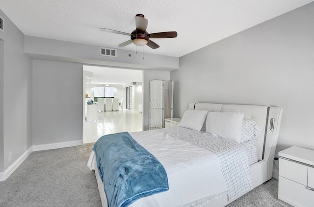 bedroom with a textured ceiling, light colored carpet, and ceiling fan