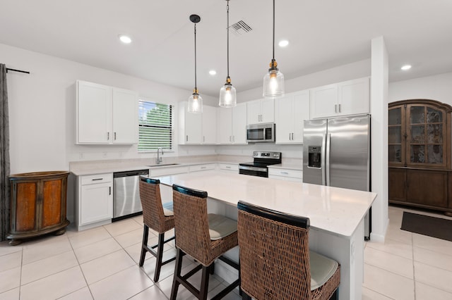 kitchen with a kitchen bar, appliances with stainless steel finishes, decorative light fixtures, a center island, and white cabinetry