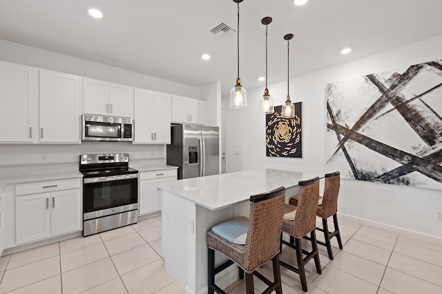 kitchen with hanging light fixtures, a kitchen island, a breakfast bar area, white cabinets, and appliances with stainless steel finishes