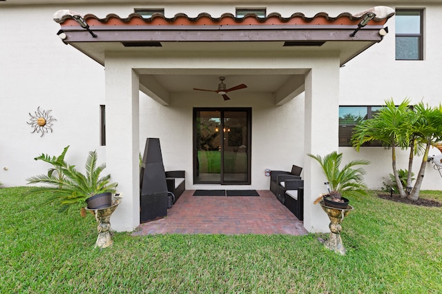 entrance to property featuring a lawn, ceiling fan, and a patio area