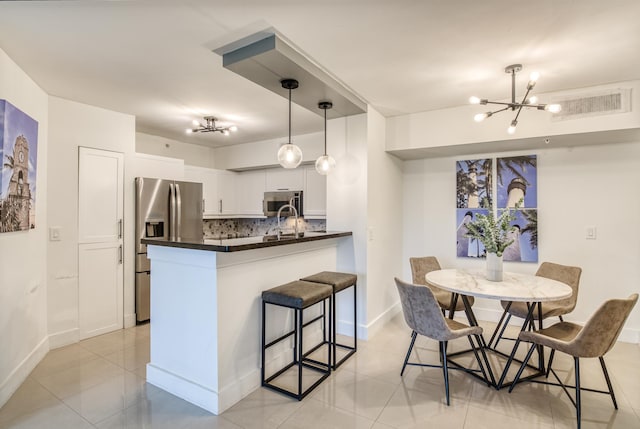 kitchen featuring appliances with stainless steel finishes, backsplash, a breakfast bar, decorative light fixtures, and white cabinets